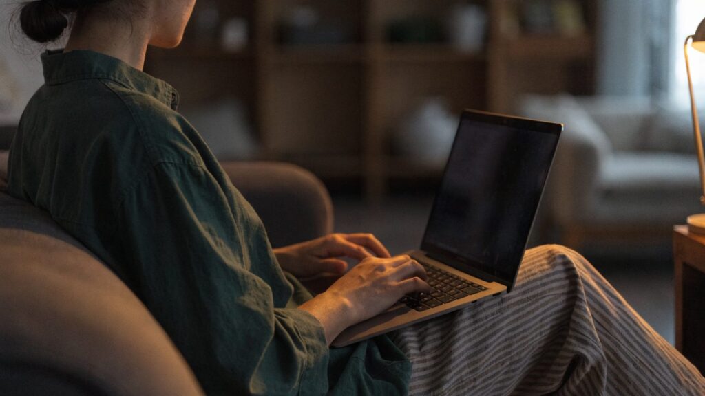 A person seen from behind using a graphite black laptop on a sofa