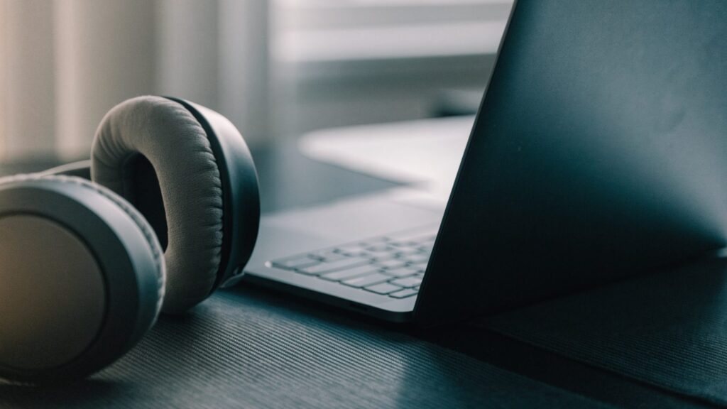 Over-ear headphones resting beside a graphite black laptop on a dark desk mat
