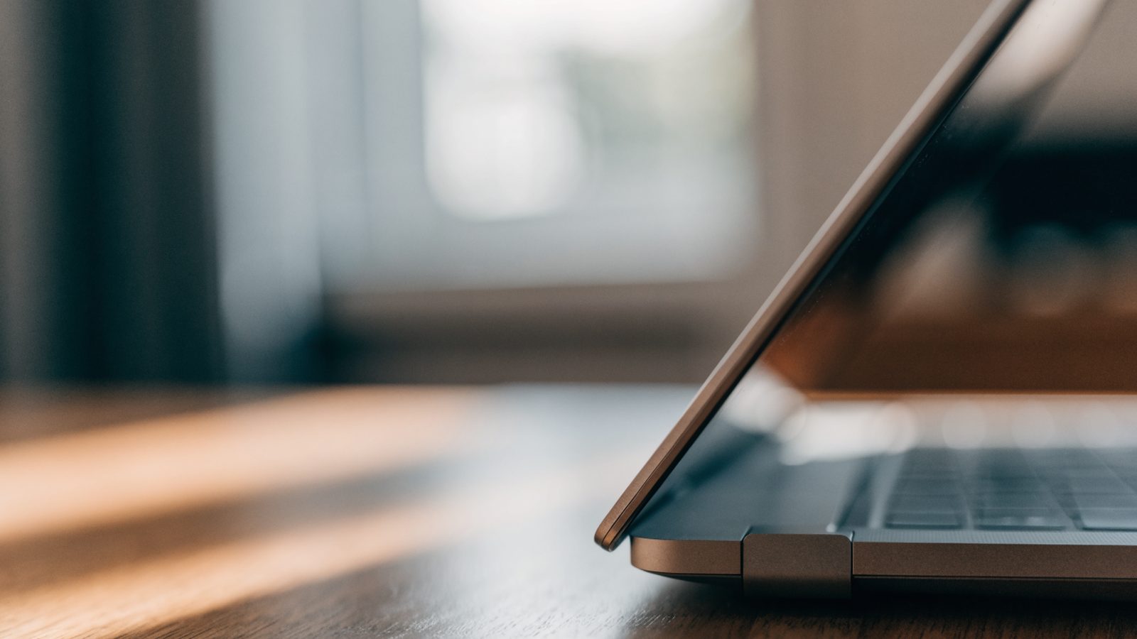 Close-up of the hinge and screen edge of a matte grey laptop on a wooden desk