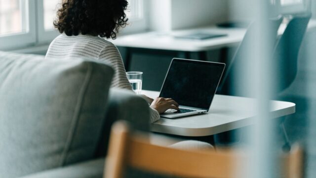 A person seen from behind working on a silver laptop in a bright home office
