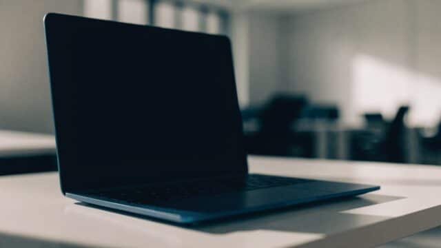 A dark blue laptop on a white desk with a completely dark blank screen