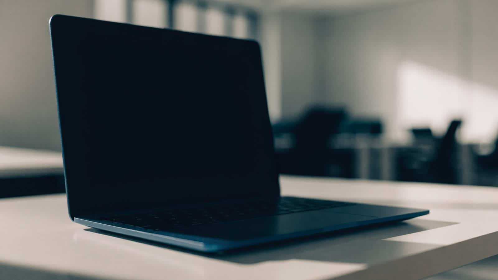A dark blue laptop on a white desk with a completely dark blank screen