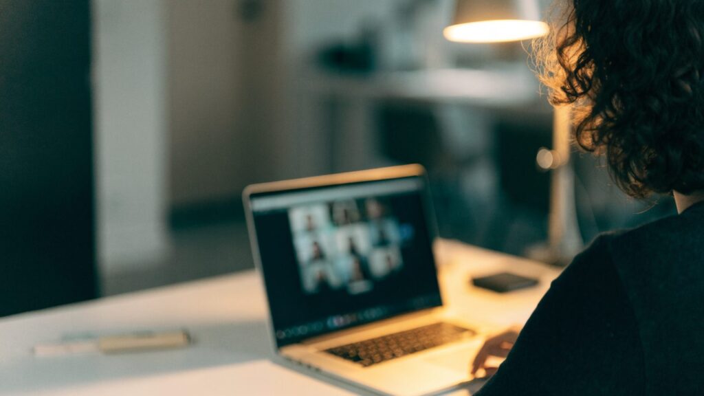 A person seen from behind on a video call on a silver laptop on a white desk