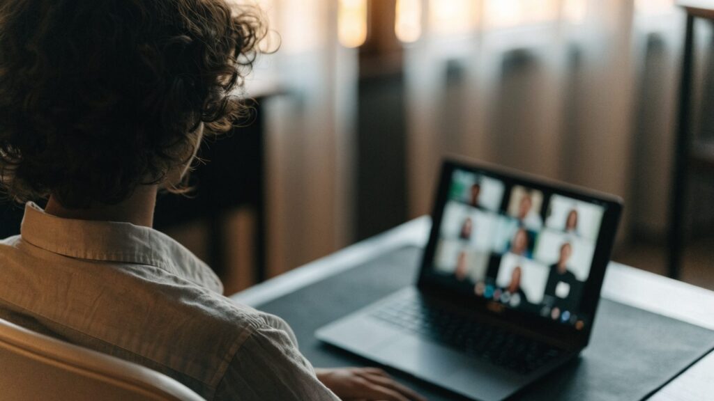 A person seen from behind on a video call on a graphite black laptop on a dark desk mat