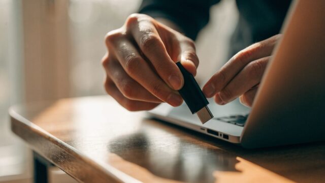 Hands unplugging a charging cable from a slim silver laptop on a wooden desk
