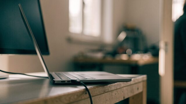 A matte grey laptop connected to a large external monitor with a blank dark screen via a cable on a workbench