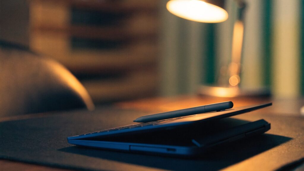 A stylus pen resting on a 2-in-1 dark blue laptop in tablet mode on a dark desk mat