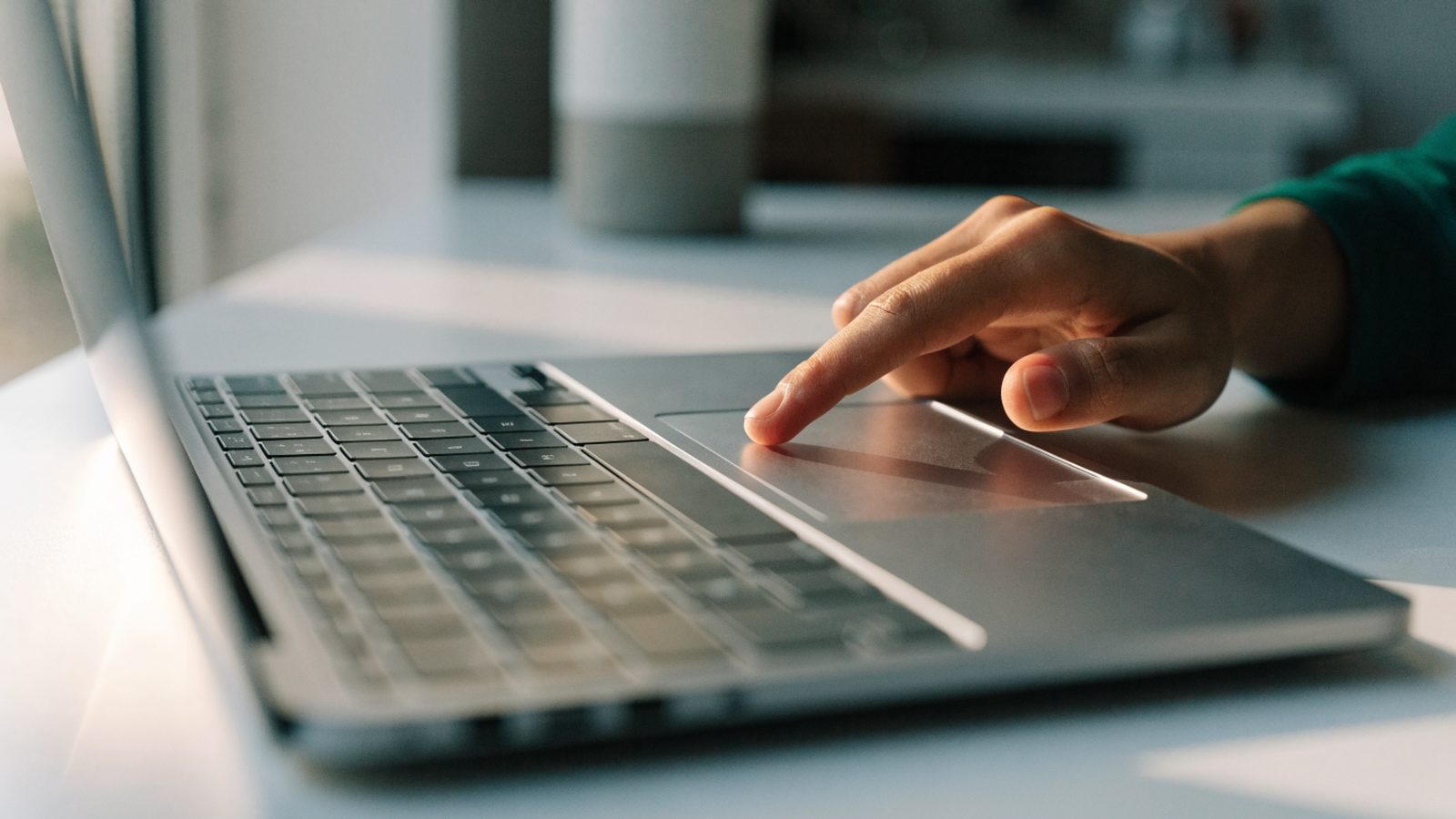 A finger gliding on the touchpad of a silver laptop on a white desk