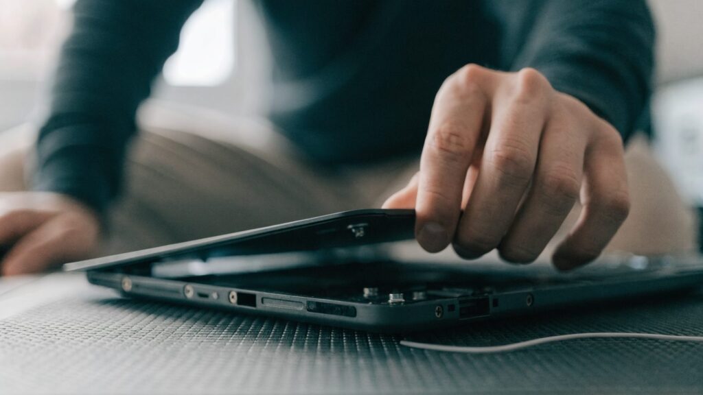 A technician lifting the bottom cover off a graphite black laptop on an anti-static mat