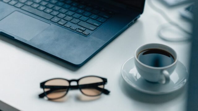 Top-down view of a dark blue laptop on a white desk with a coffee cup and glasses