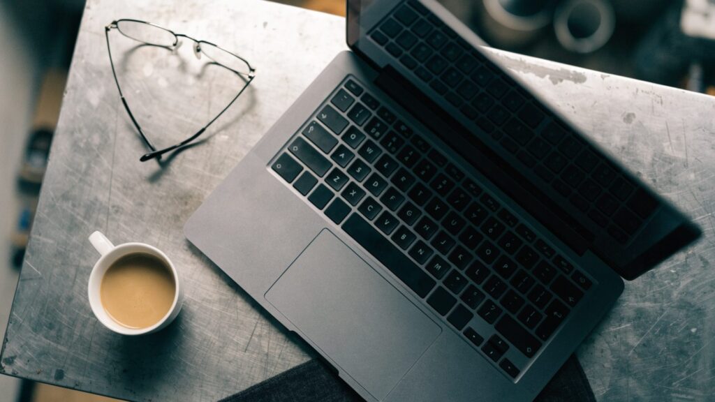 Top-down view of a matte grey laptop on a workbench with a coffee cup and glasses