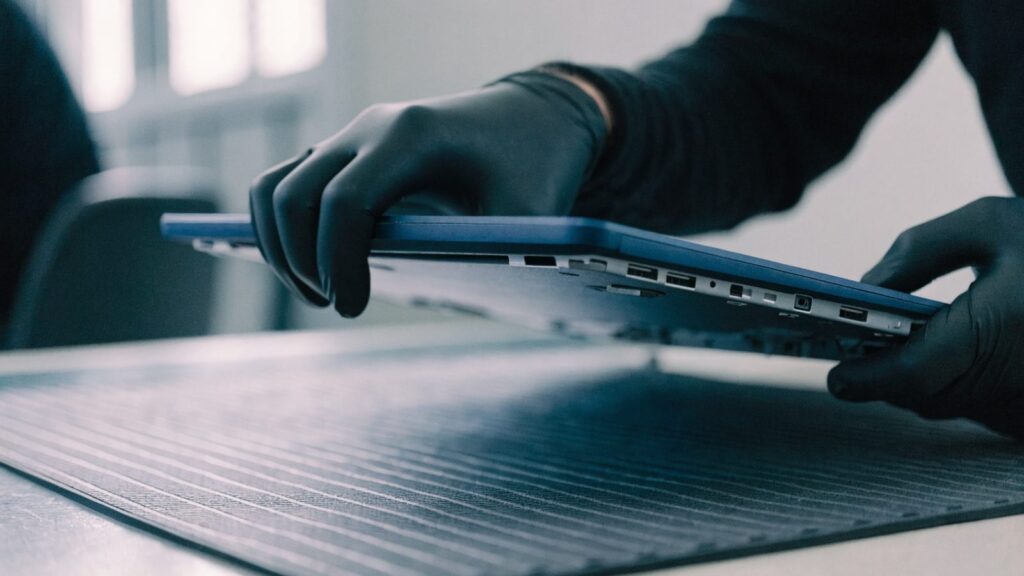 A technician lifting the bottom cover off a dark blue laptop on an anti-static mat