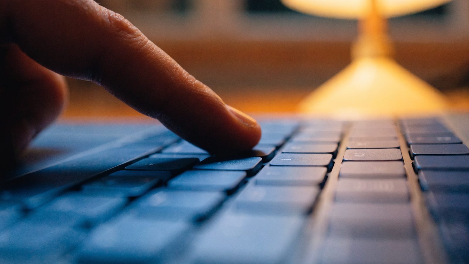 Close-up of a single key being pressed on a dark blue laptop keyboard