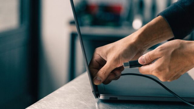 Hands unplugging a charging cable from a slim graphite black laptop on a workbench