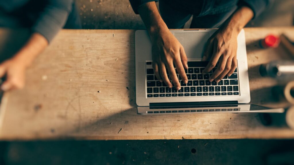 Hands typing on the keyboard of a silver laptop on a workbench