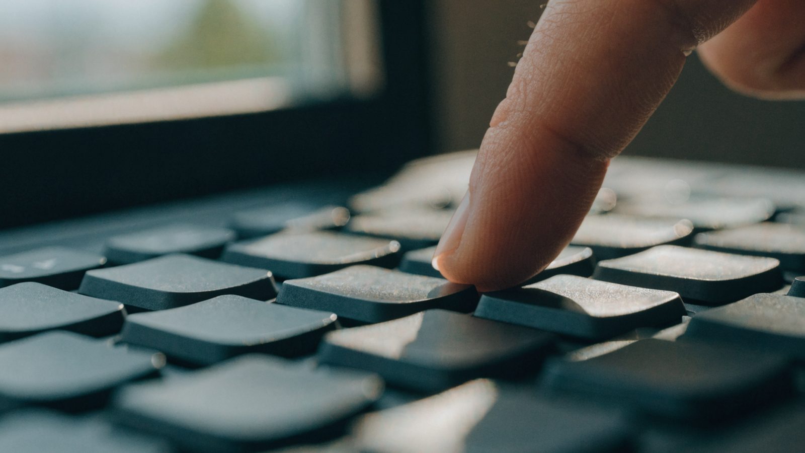 Close-up of a single key being pressed on a graphite black laptop keyboard