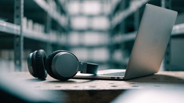 Over-ear headphones resting beside a silver laptop on a workbench