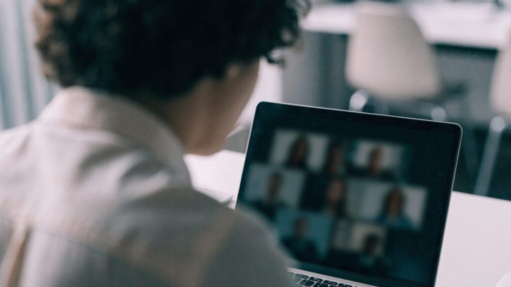 A person seen from behind on a video call on a silver laptop on a white desk