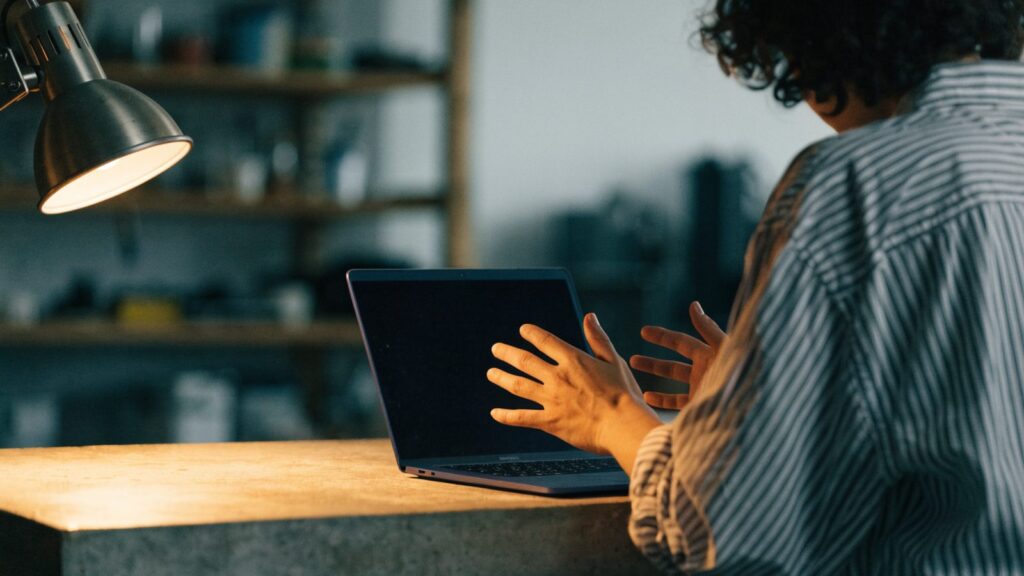 A person seen from behind with hands raised at a dark blue laptop with a dark blank screen on a workbench