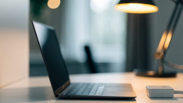 A graphite black laptop on a white desk next to a compact white power adapter with its cable neatly coiled