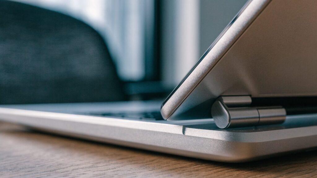 A person seen from behind with hands raised at a graphite black laptop with a dark blank screen on an office d