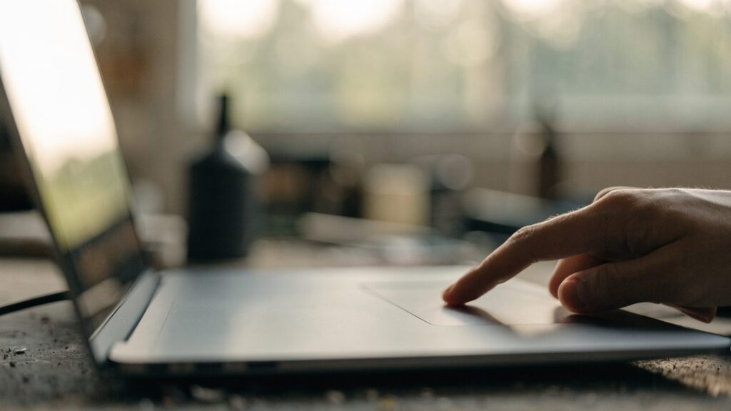 A finger gliding on the touchpad of a matte grey laptop on a workbench