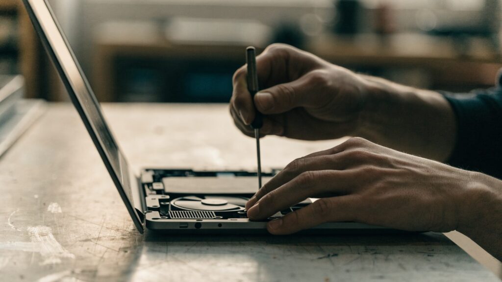 A technician's hands holding a small screwdriver over an opened graphite black laptop with internal components