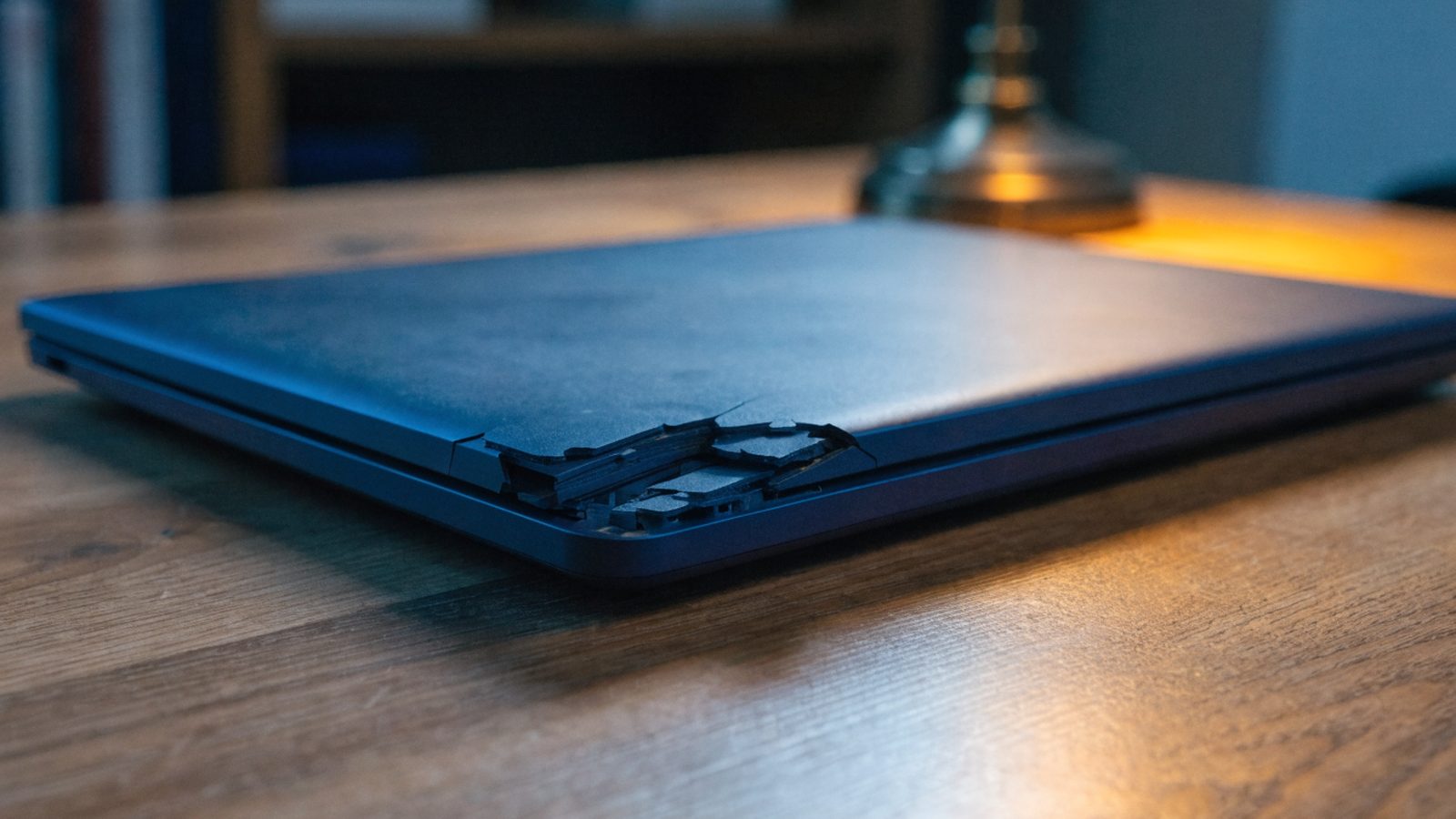 Close-up of a cracked corner on a closed dark blue laptop on a wooden desk