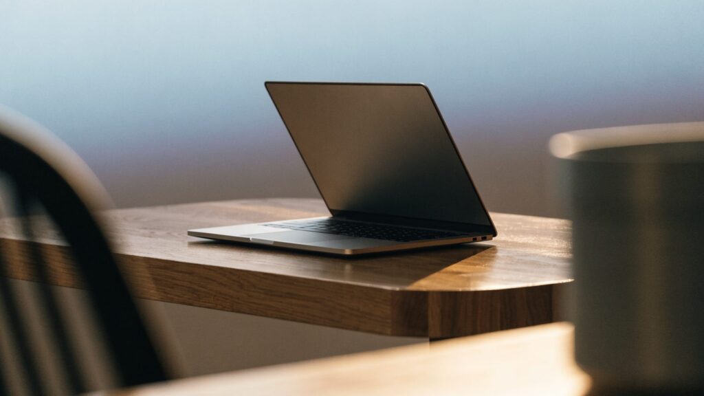 A sleek modern silver laptop centered on a wooden desk against a clean soft gradient background