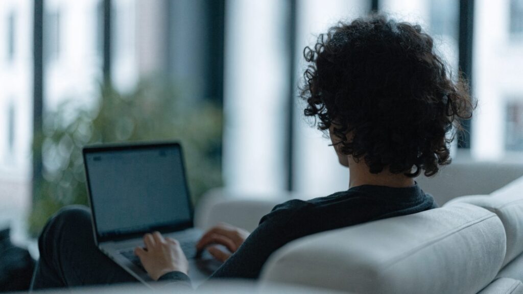 A person seen from behind using a matte grey laptop on a sofa