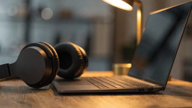 Over-ear headphones resting beside a graphite black laptop on a wooden desk