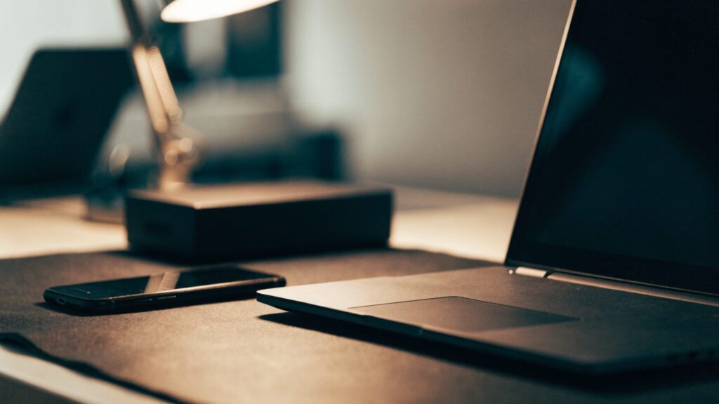A smartphone lying beside a graphite black laptop on a dark desk mat