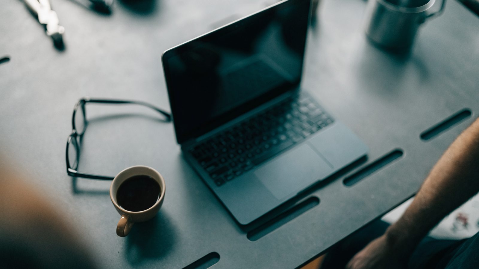 Top-down view of a matte grey laptop on a workbench with a coffee cup and glasses