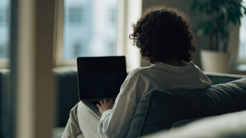 A person seen from behind using a matte grey laptop on a sofa