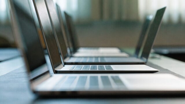 Several modern laptops lined up in a row on a dark desk mat