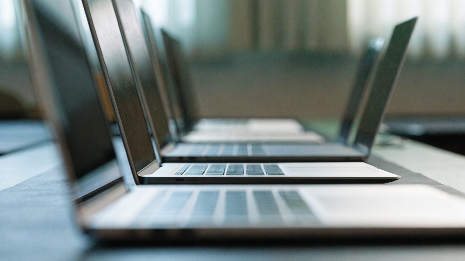Several modern laptops lined up in a row on a dark desk mat
