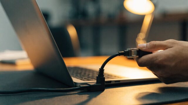 An ethernet cable being plugged into a USB-C adapter connected to a silver laptop on a dark desk mat
