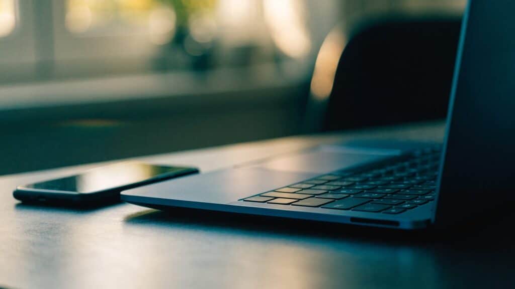 A smartphone lying beside a dark blue laptop on a dark desk mat