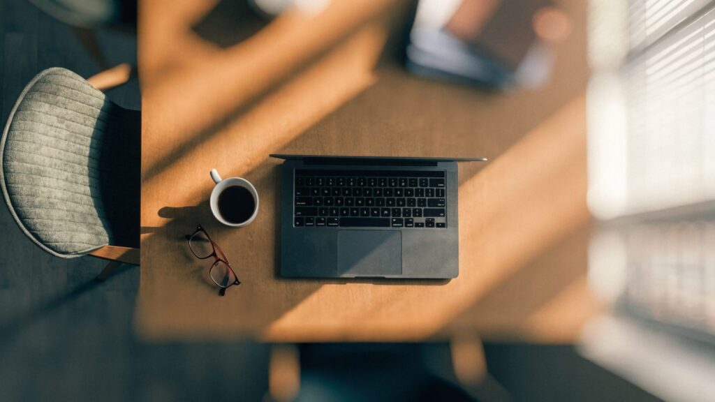 Top-down view of a matte grey laptop on an office desk with a coffee cup and glasses