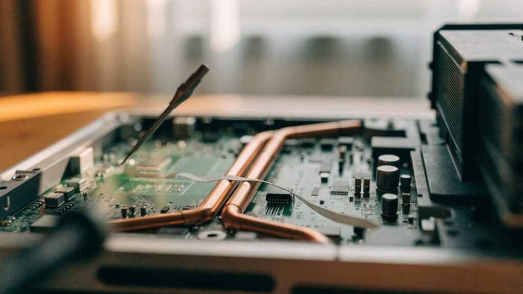 Close-up of a laptop motherboard with copper heat pipes during a repair