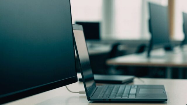 A graphite black laptop connected to a large external monitor with a blank dark screen via a cable on an offic
