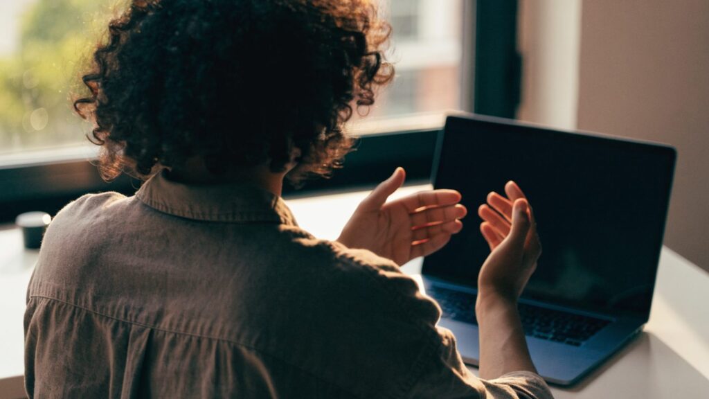 A person seen from behind with hands raised at a dark blue laptop with a dark blank screen on a white desk