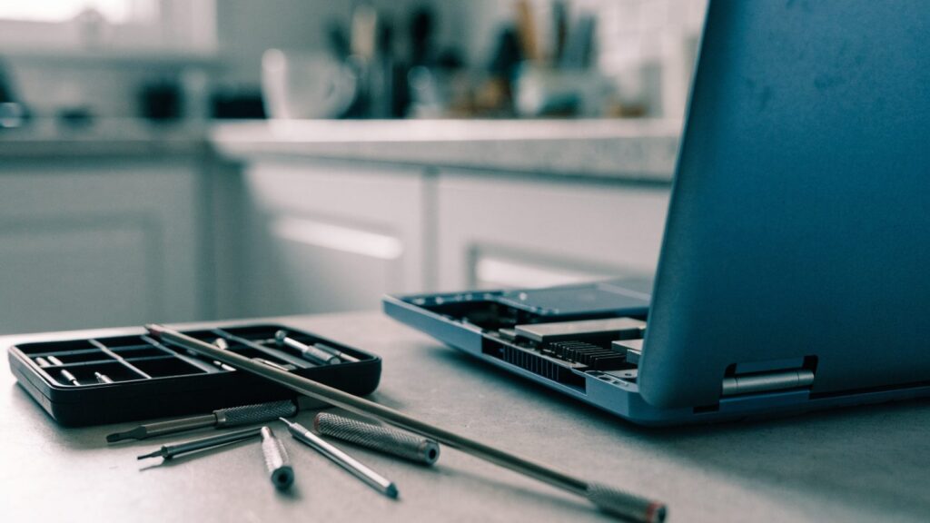 A precision screwdriver kit laid out beside a partially opened dark blue laptop on a kitchen table