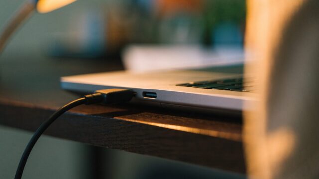 Close-up of a USB-C charger cable plugged into the side port of a silver laptop on an office desk
