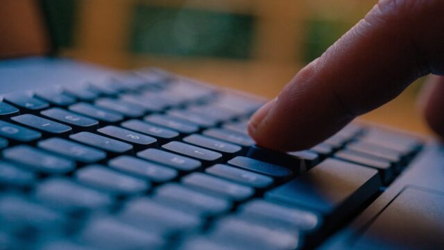 Close-up of a single key being pressed on a dark blue laptop keyboard