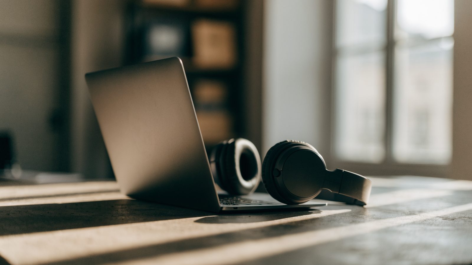 Over-ear headphones resting beside a matte grey laptop on a workbench