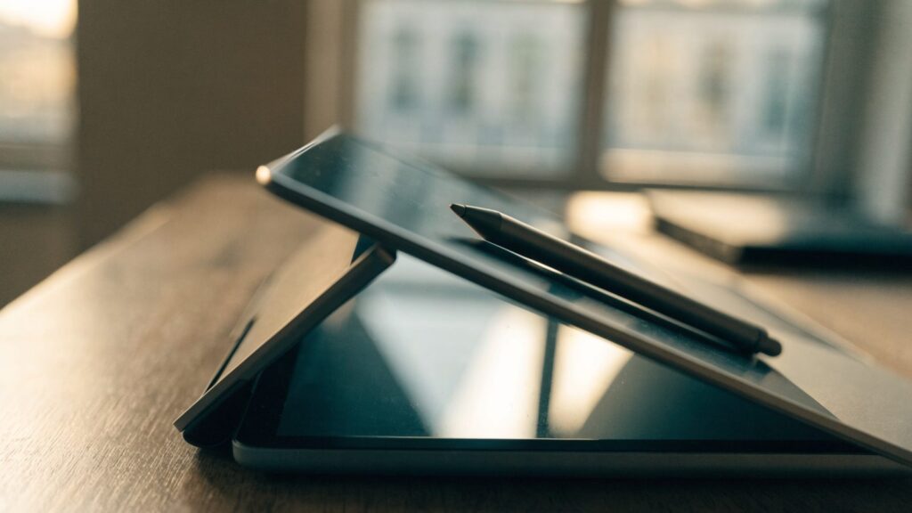 A stylus pen resting on a 2-in-1 graphite black laptop in tablet mode on a wooden desk