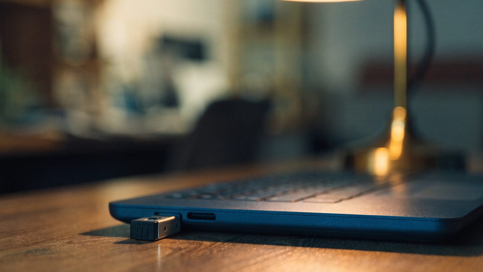 A USB flash drive plugged into the side port of a dark blue laptop on a wooden desk