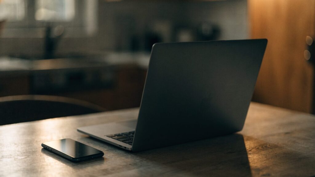 A smartphone lying beside a graphite black laptop on a kitchen table
