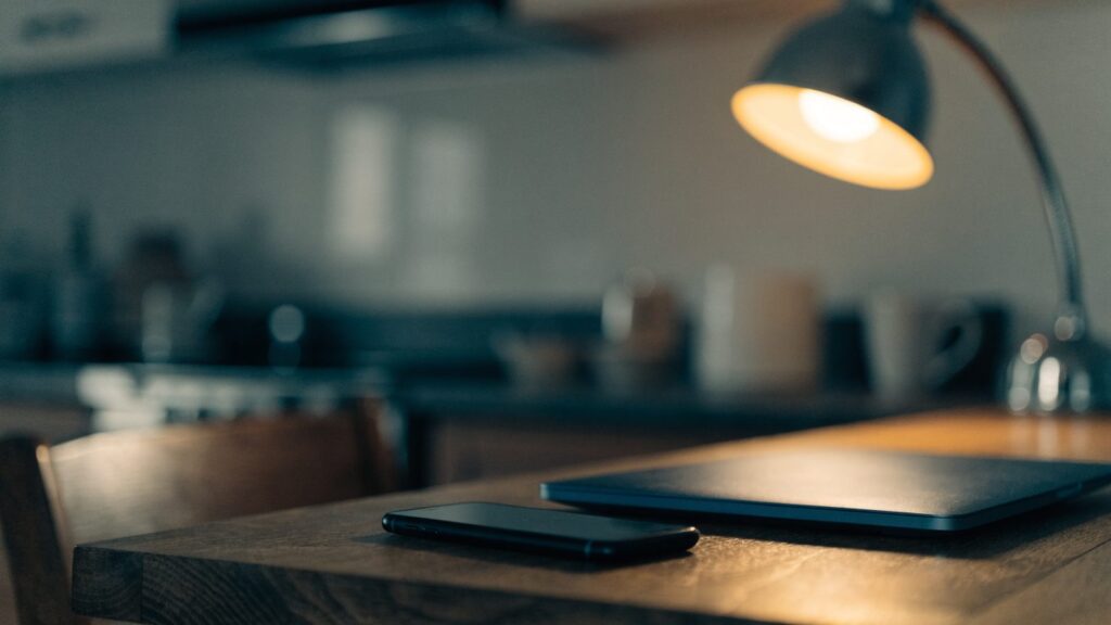 A smartphone lying beside a dark blue laptop on a kitchen table